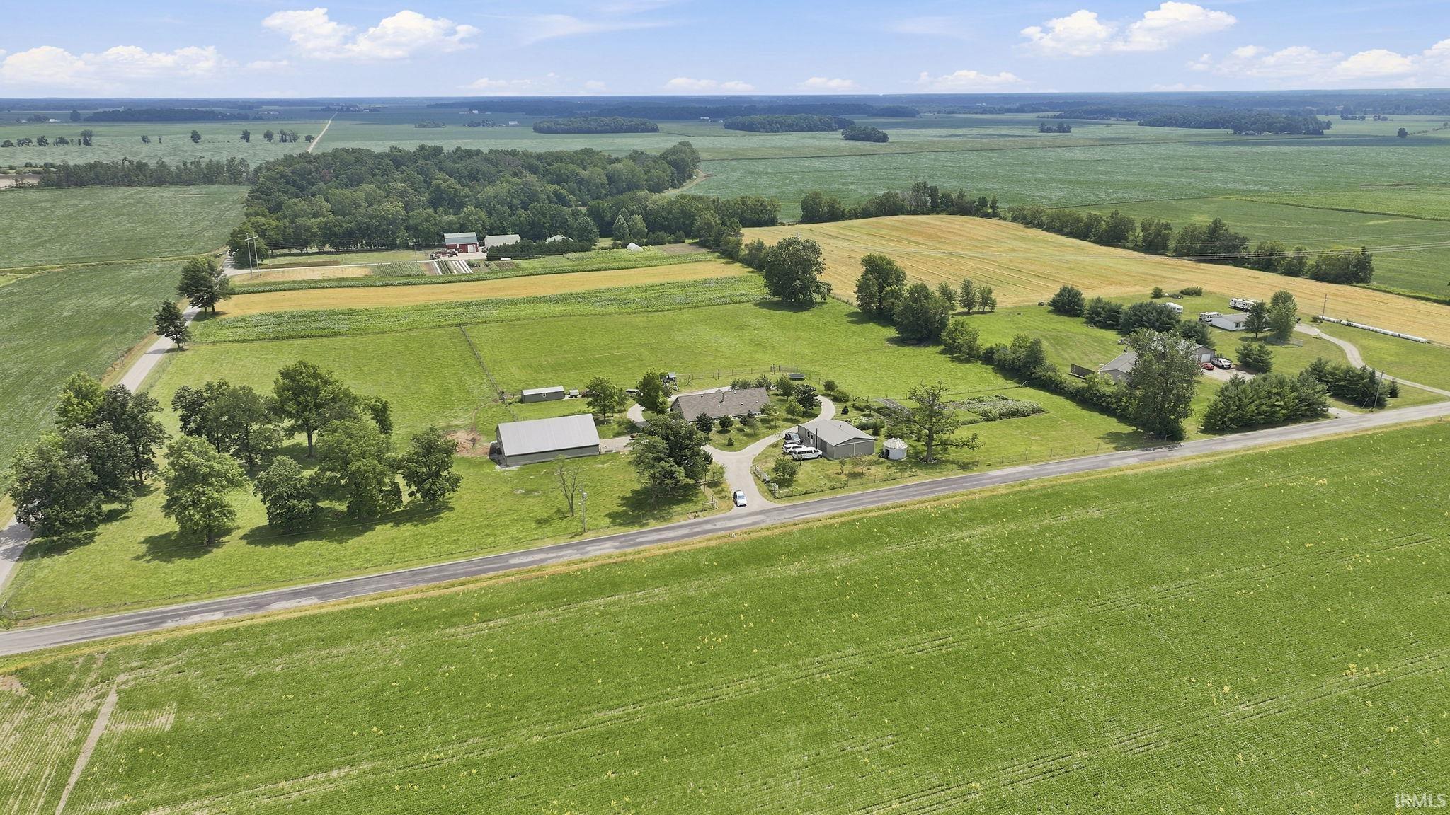 Expansive agricultural property featuring multiple buildings, cultivated fields, mature trees, and a paved road frontage