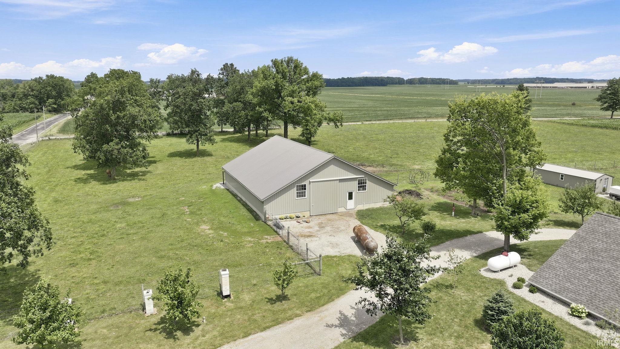 Expansive agricultural property featuring a large light green barn with a gray metal roof, gravel driveway, mature trees, and surrounding open fields
