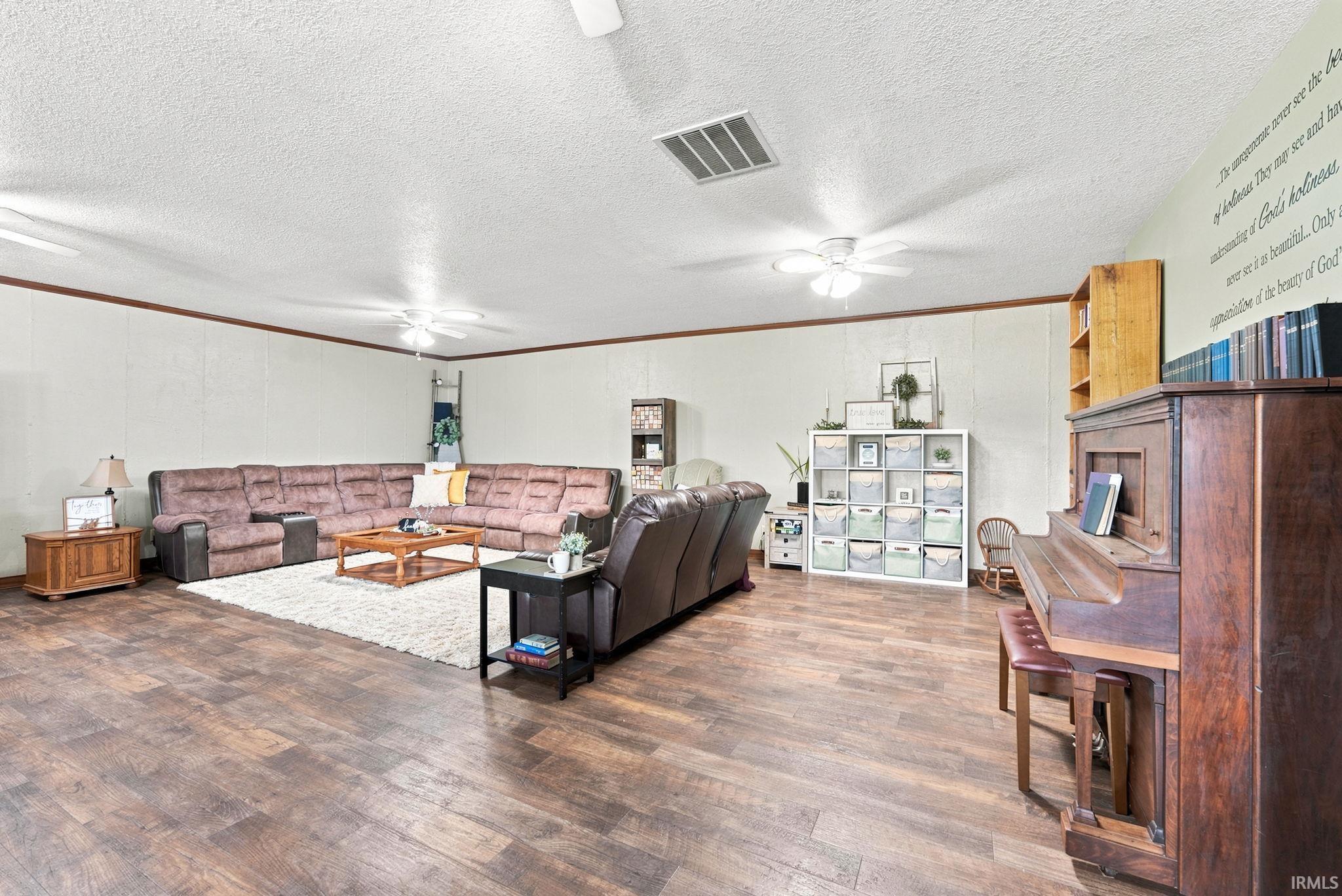 Spacious living area featuring wood-finish flooring, light-colored walls with dark trim, and multiple ceiling fans for circulation