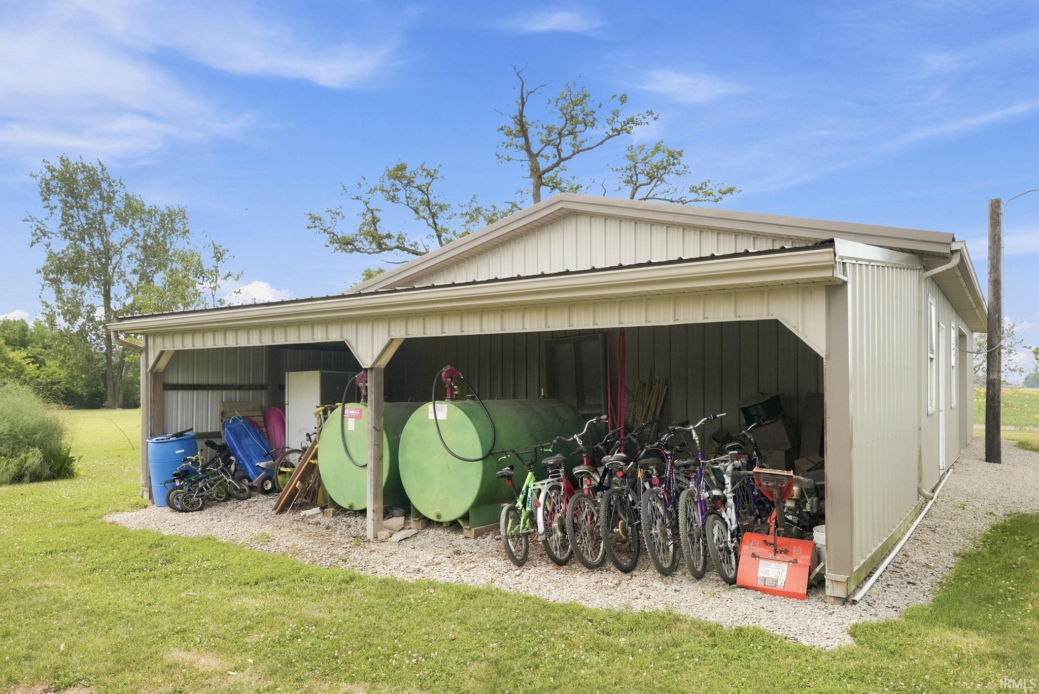 Metal-sided utility building featuring a covered open-air storage area, a closed storage section with windows, a pitched roof, and gravel ground cover