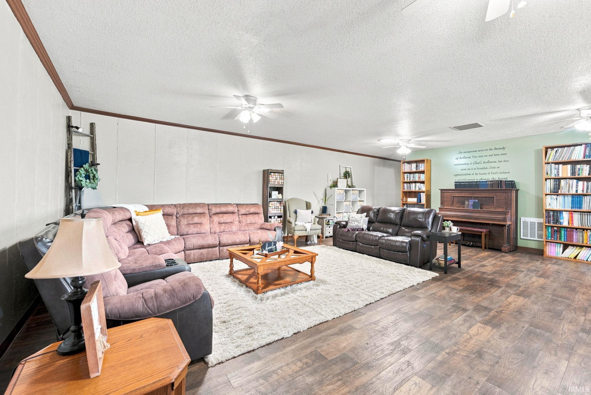 Spacious living area featuring wood-finish flooring, a light-colored accent wall, and multiple ceiling fans