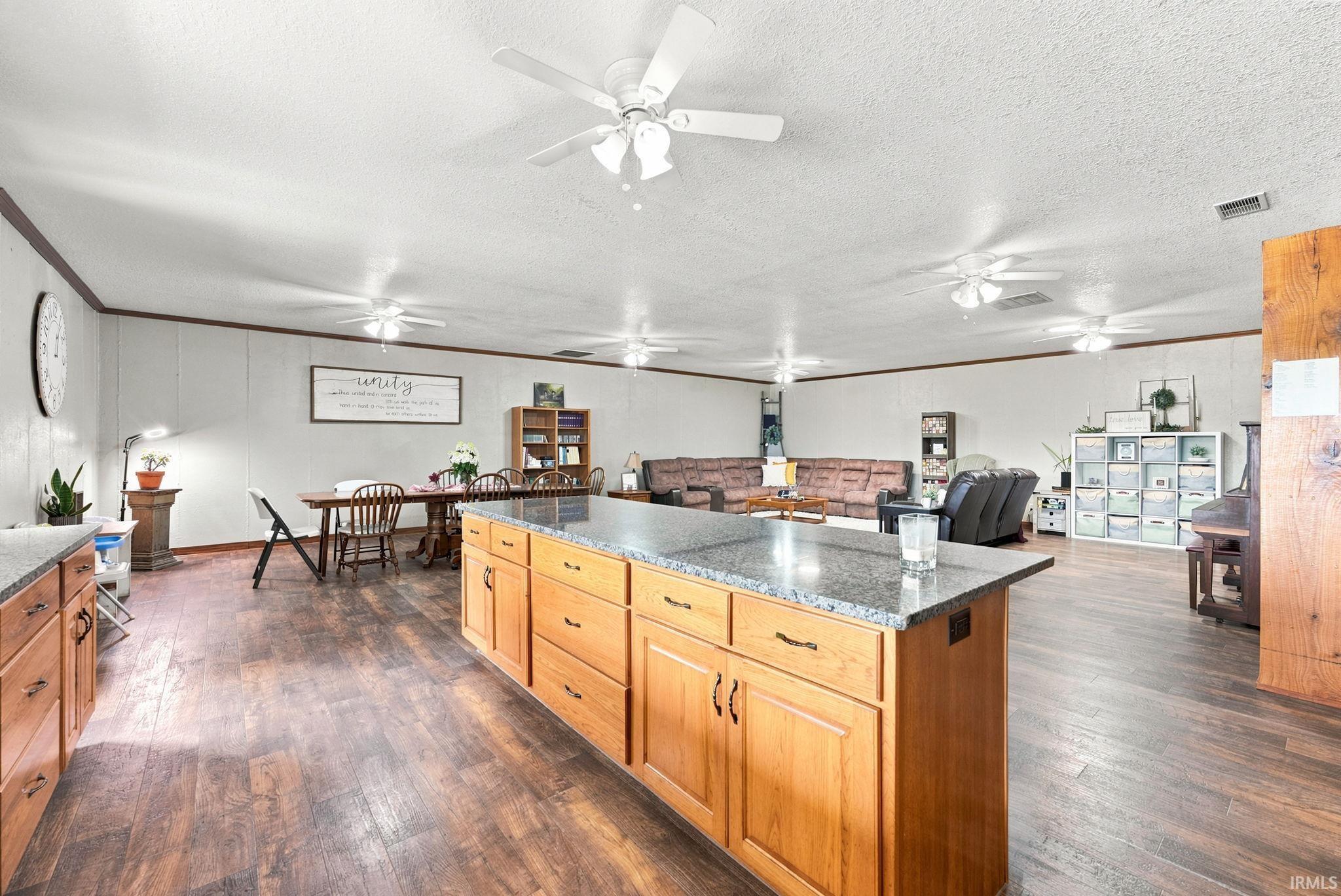 Spacious room featuring wood-finish flooring, a kitchen island with a stone countertop, abundant ceiling fans, and built-in cabinetry