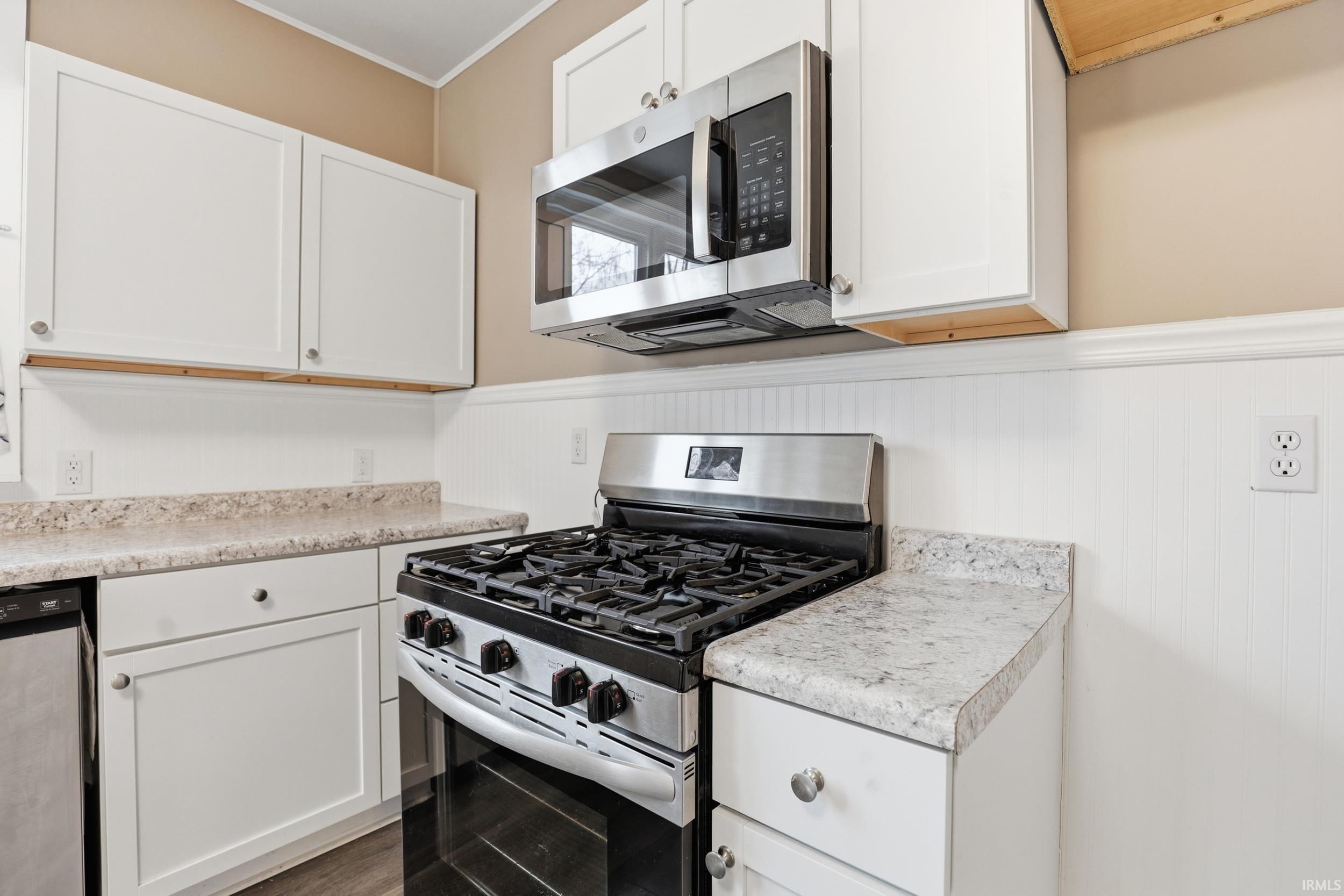 Kitchen with stainless steel appliances, wainscoting, light countertops, white cabinetry, and crown molding