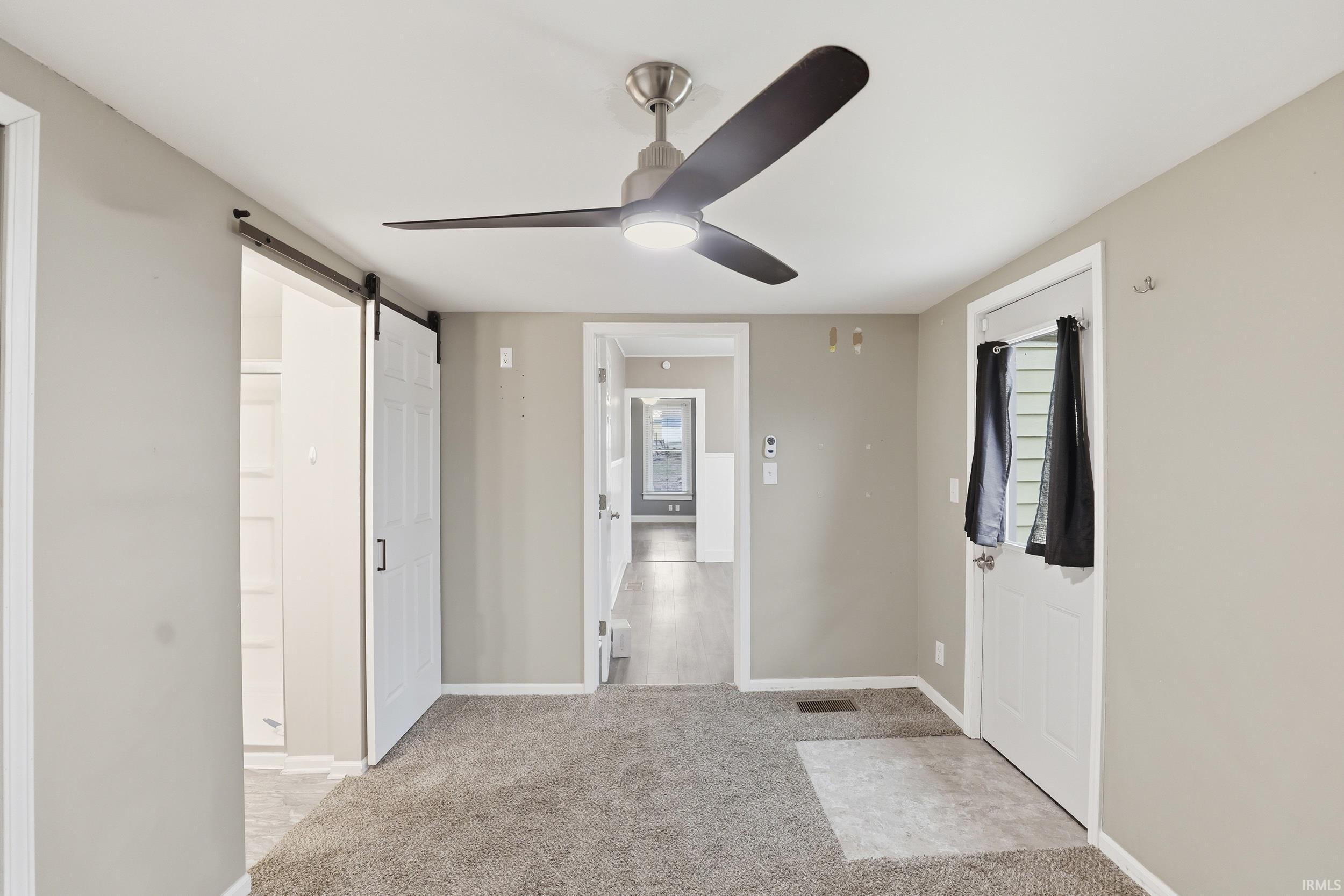 Entrance foyer with a barn door, light colored carpet, and ceiling fan