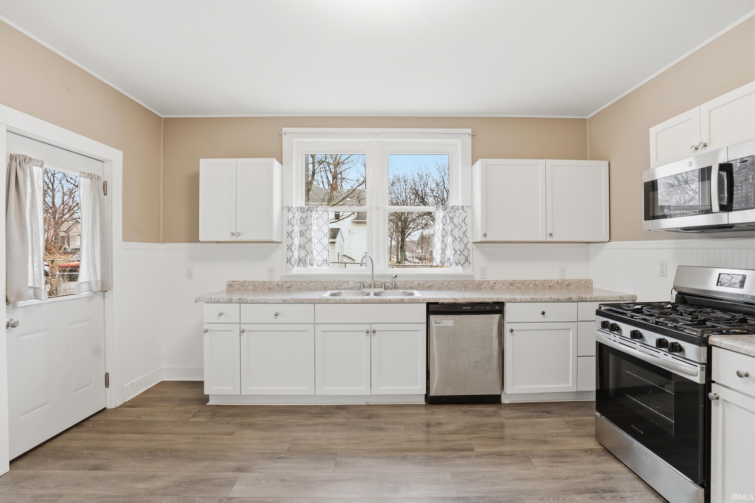 Kitchen featuring stainless steel appliances, wainscoting, white cabinetry, light countertops, and light wood-type flooring