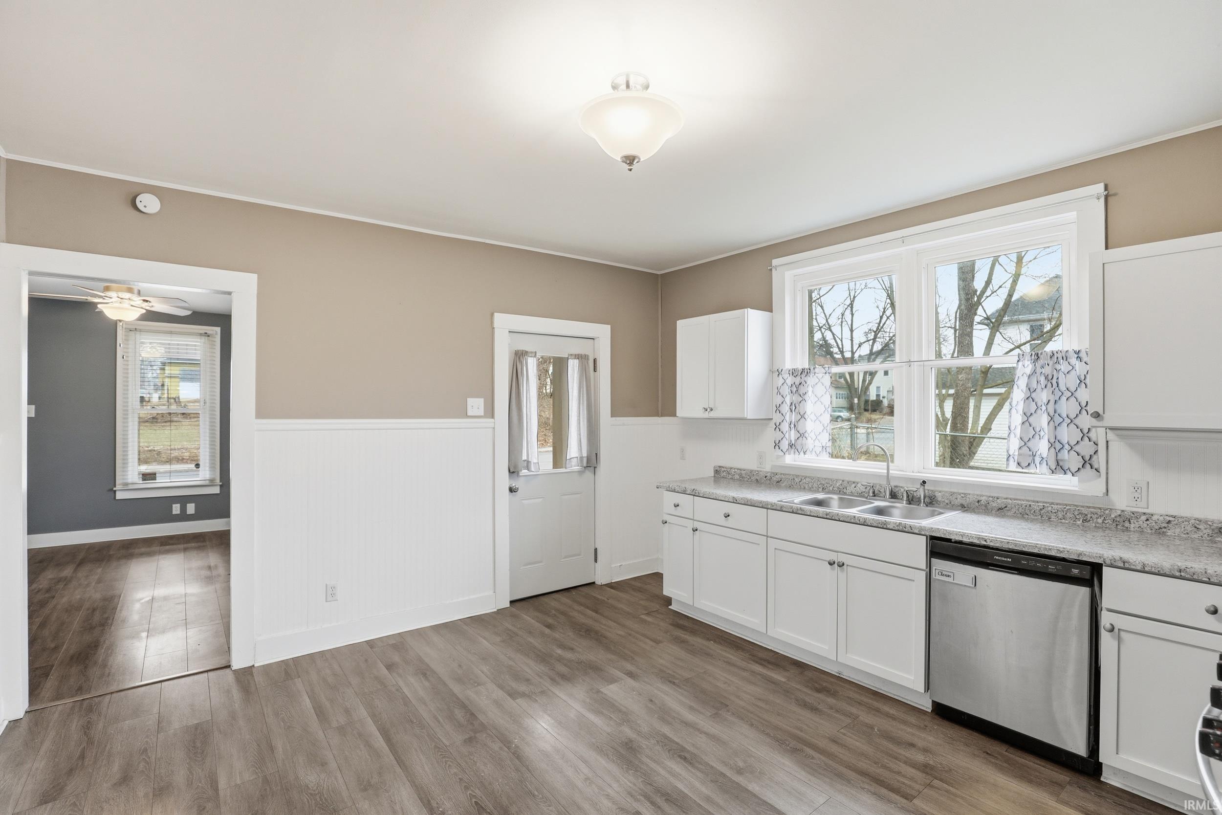 Kitchen featuring a wainscoted wall, stainless steel dishwasher, white cabinetry, light countertops, and light wood-type flooring