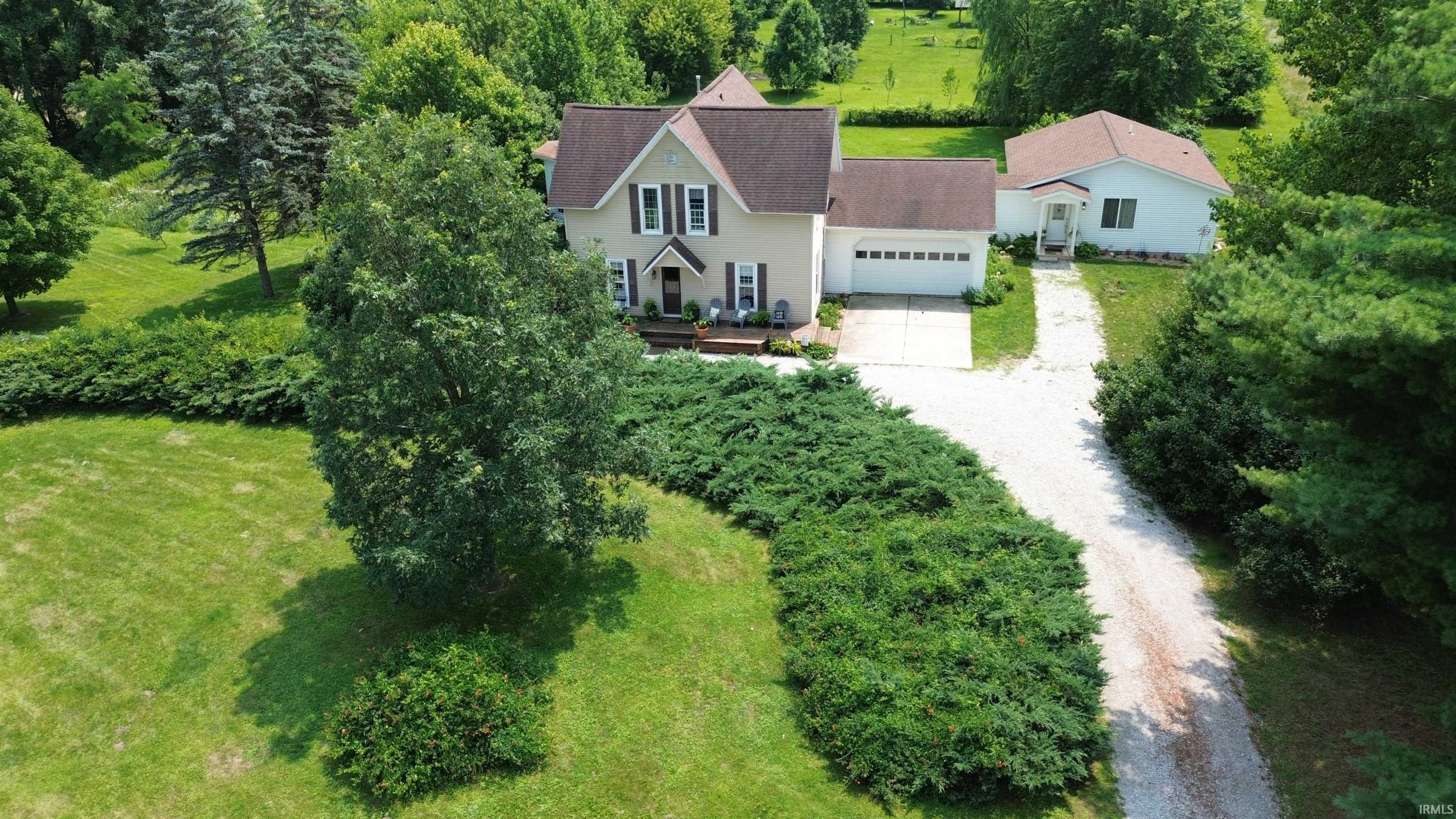 Two-story residence featuring a two-car garage, a separate outbuilding, a gravel driveway, mature trees, and landscaping