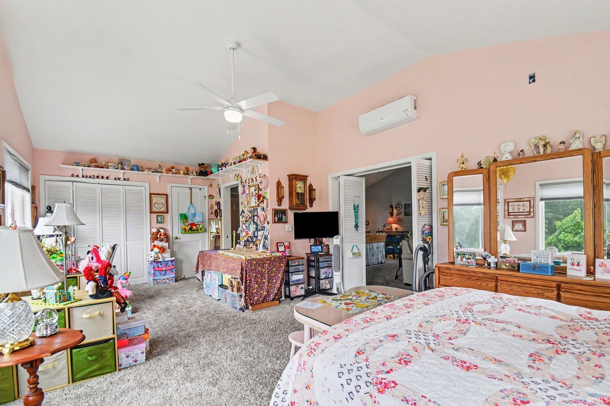 Spacious room featuring vaulted ceilings, a ceiling fan, carpet flooring, and dual bi-fold closet doors