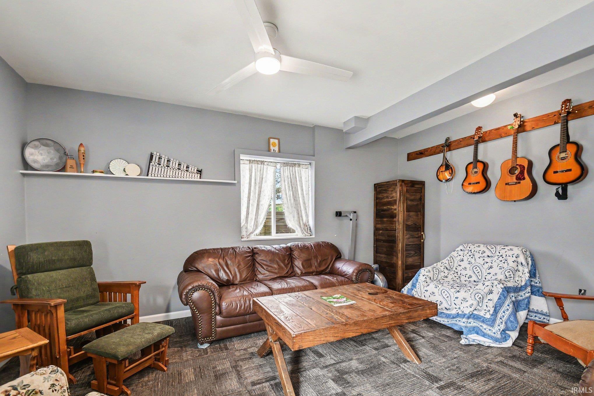 Spacious room featuring gray painted walls, wood-finish flooring, a ceiling fan with integrated lighting, and a white floating wall shelf
