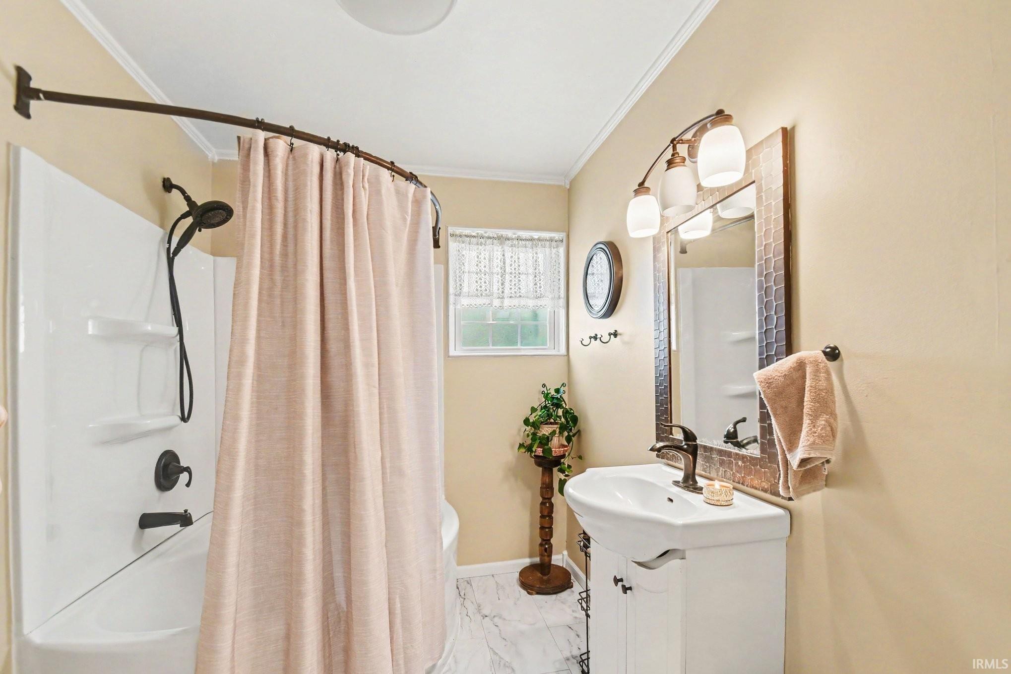 Bathroom featuring a combination shower and tub with oil-rubbed bronze fixtures, a single vanity with a white basin and dark bronze faucet, a framed mirror, and tile flooring