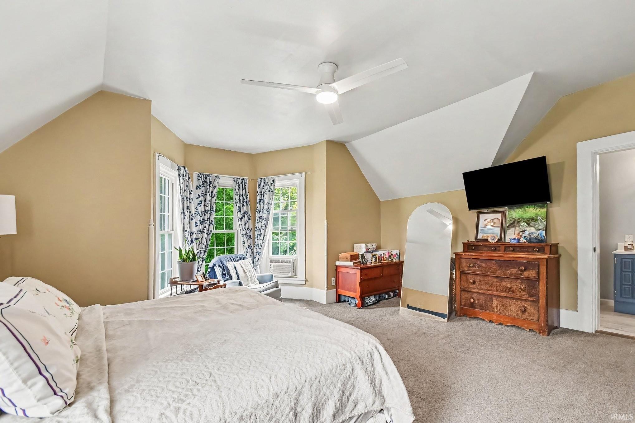 Spacious room featuring sloped ceilings, recessed bay window area, light tan wall color, and light grey carpeting
