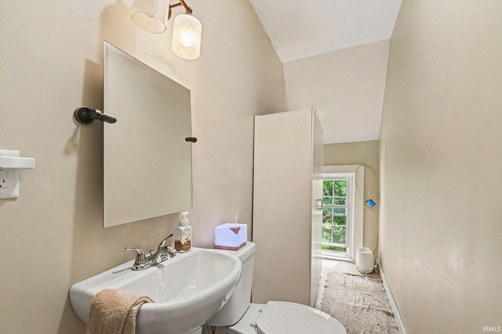 Pedestal sink with chrome fixtures, an overhead vanity light with decorative glass shades, and a frameless mirror