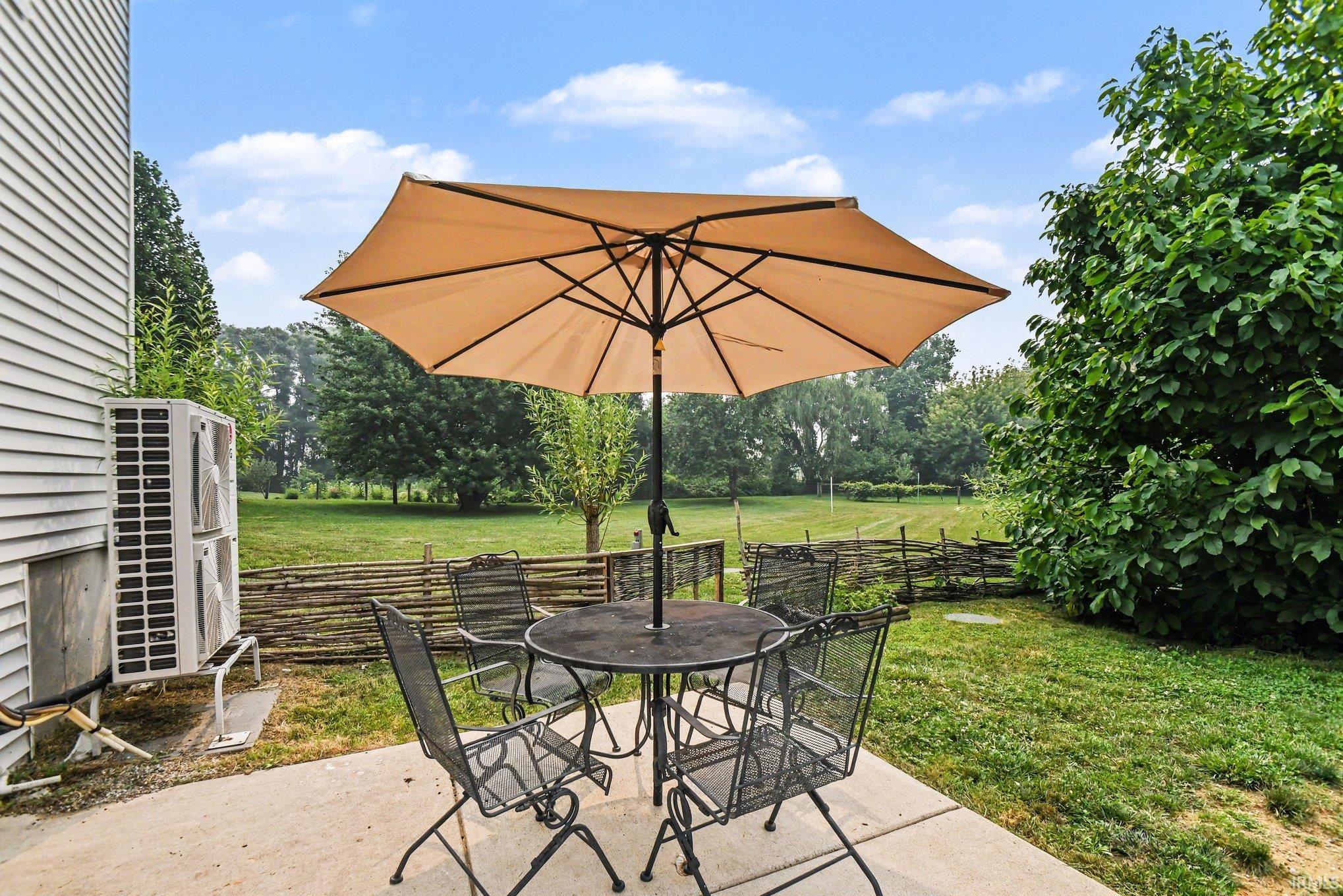 Concrete patio with expansive green space, mature trees, and natural wood fencing