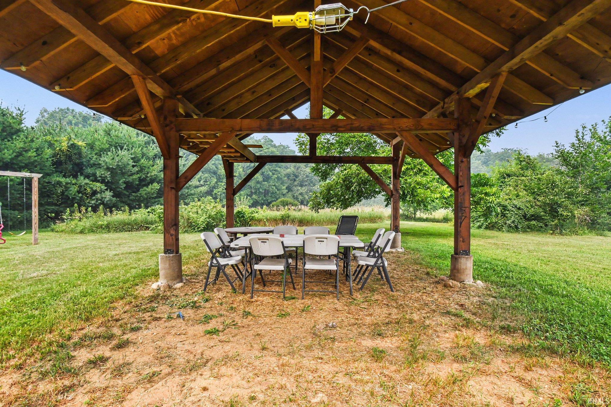 Spacious wooden gazebo with exposed rafters and a light fixture, set on a gravel base