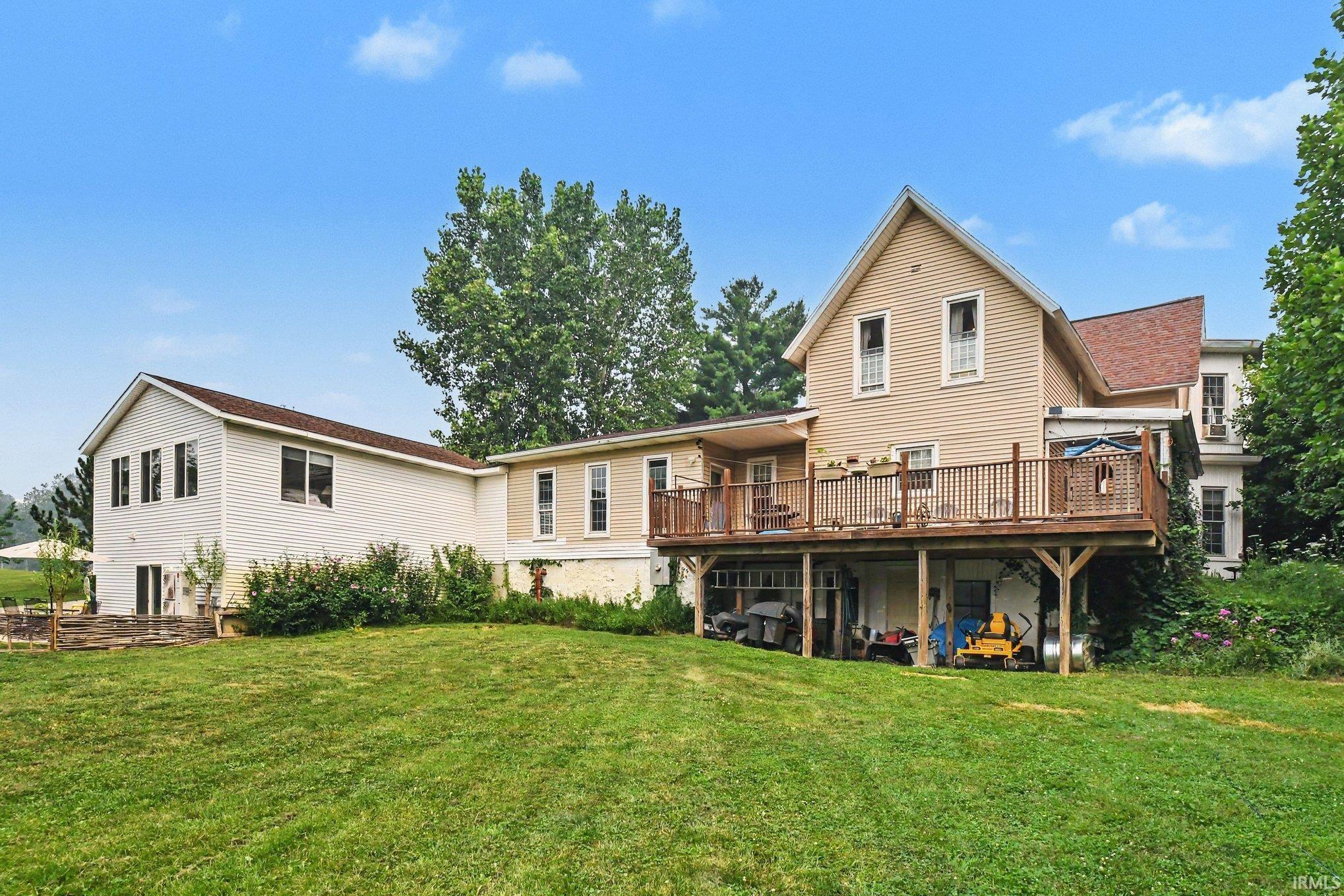 Expansive green lawn with a multi-level dwelling featuring two-story siding, multiple windows, an upper-level deck with wood railings, and a lower-level covered outdoor area