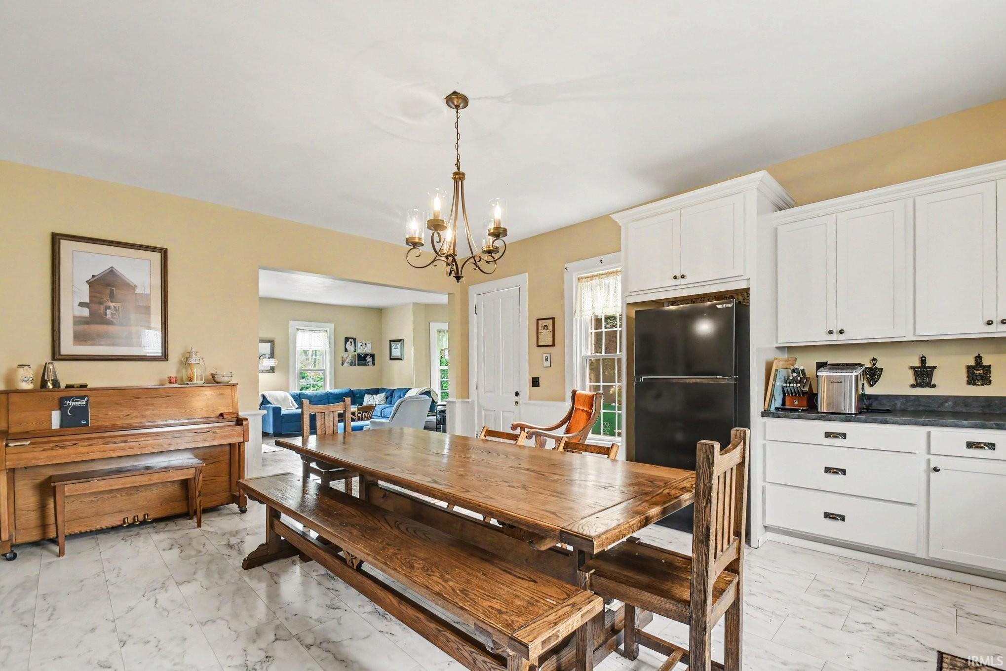 Open-concept dining area featuring a chandelier, white cabinetry, dark countertops, and light-toned flooring