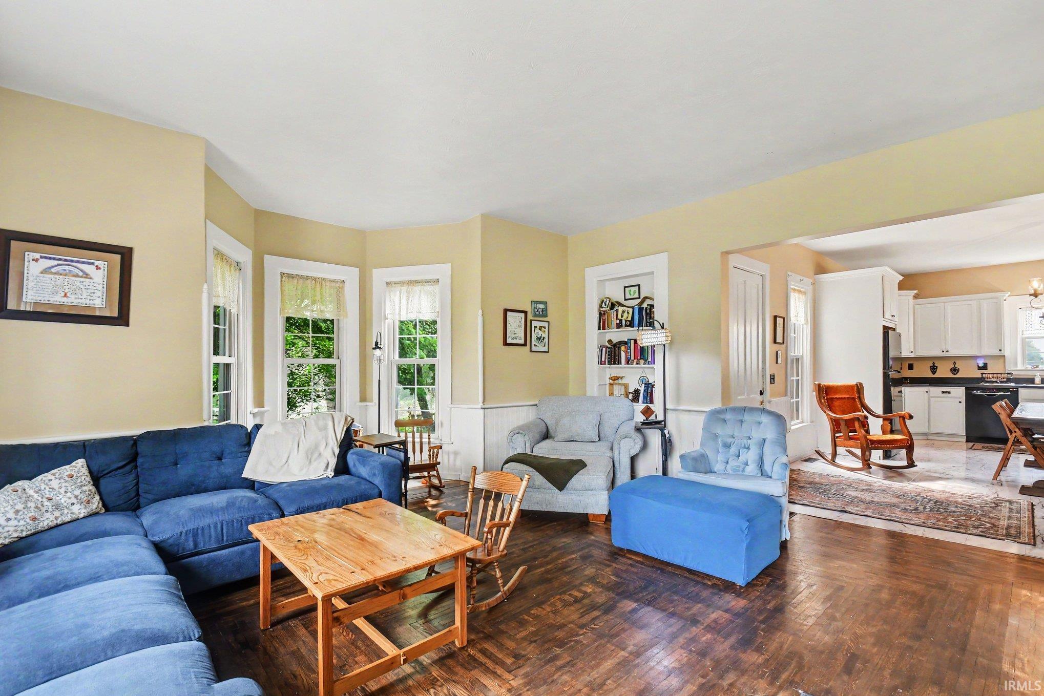 Living space featuring wood-finish flooring, a bay window with three vertical windows, and a built-in shelving unit