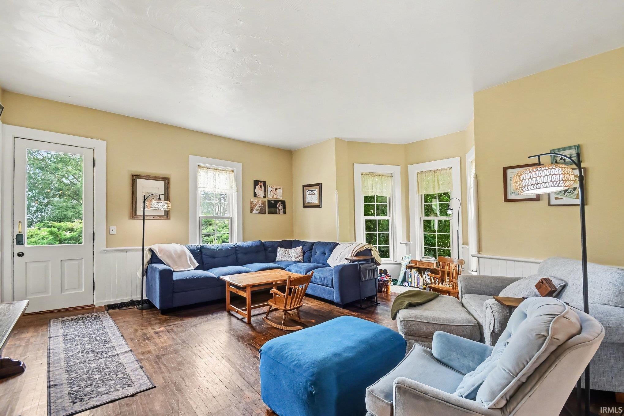 Living room featuring wood-finish flooring, light-colored walls, white trim, and a white paneled door with exterior access