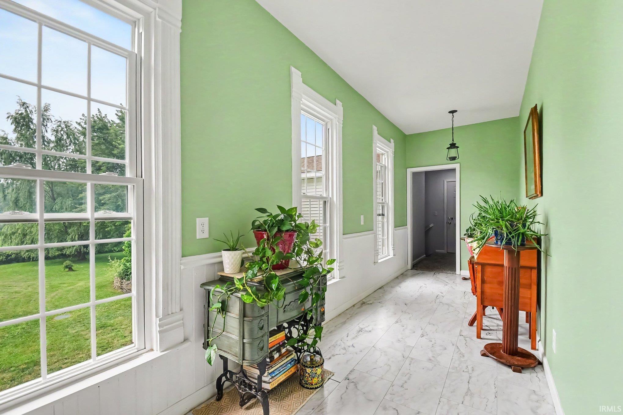 Hallway featuring light green walls, white wainscoting, and large windows with white trim