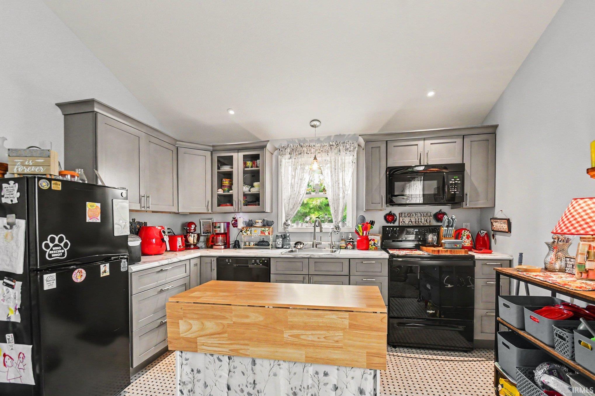 Kitchen featuring gray cabinetry, white countertops, black appliances, a central wood-finish island, and patterned flooring