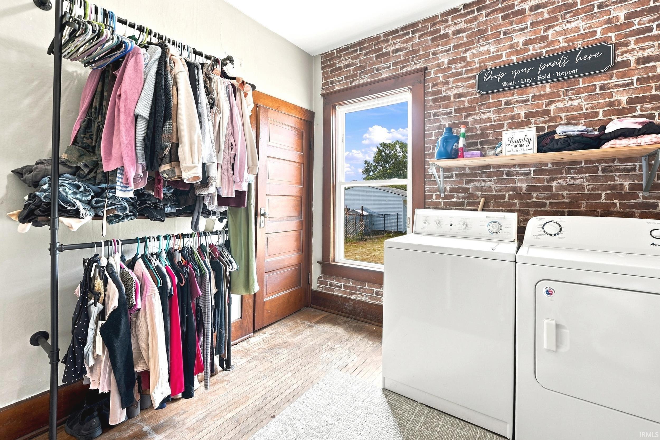 Laundry area featuring exposed brick accent wall, wood-finish flooring, and a window with wood trim