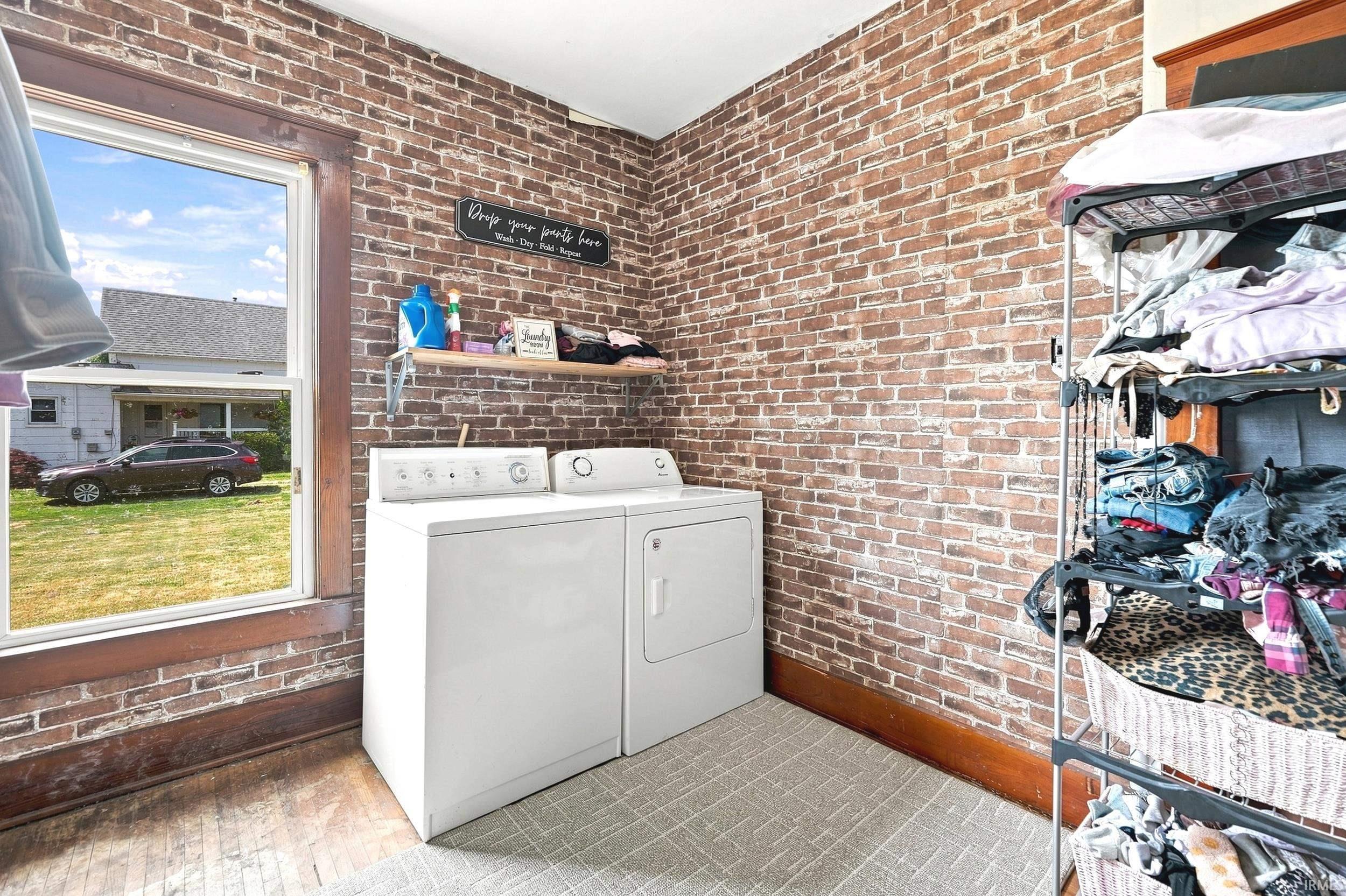 Laundry area featuring exposed brick-style wall treatment and a window with wood trim