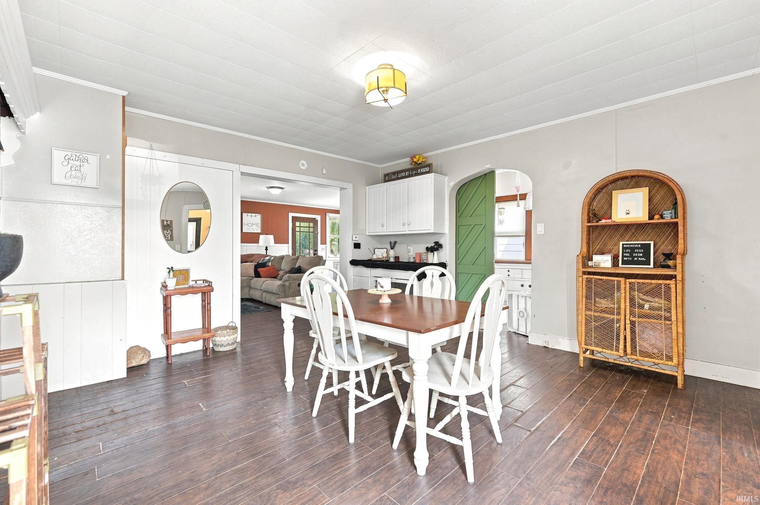 Dining area featuring wood-finish flooring, white paneling, and a decorative archway