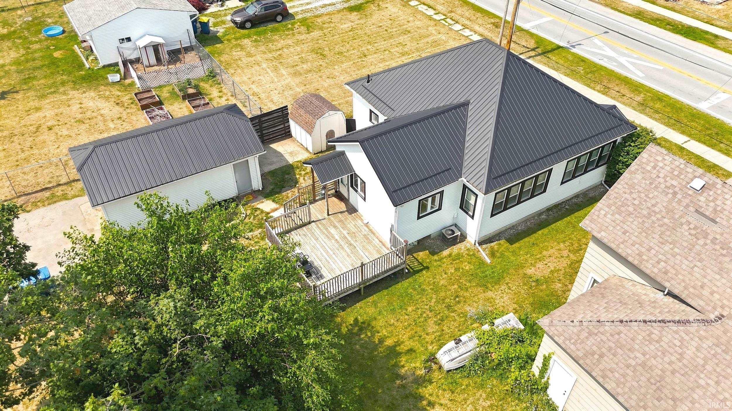 White exterior residence featuring a dark metal roof, rear deck with wood railing, detached garage with dark metal roof, and a visible storage shed
