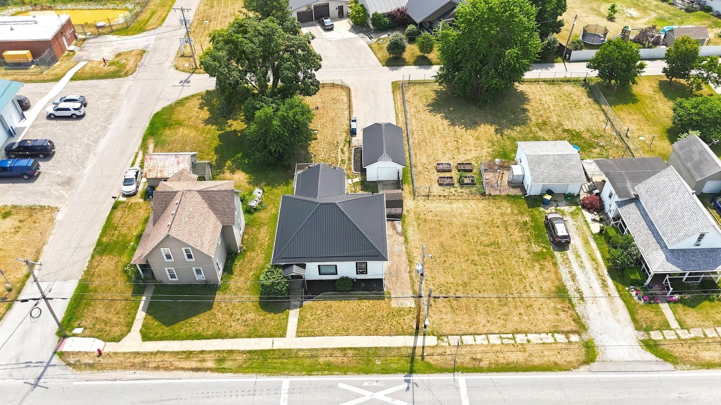 Aerial view of a residential property with a dark-pitched roof and light-colored siding, featuring a detached garage structure