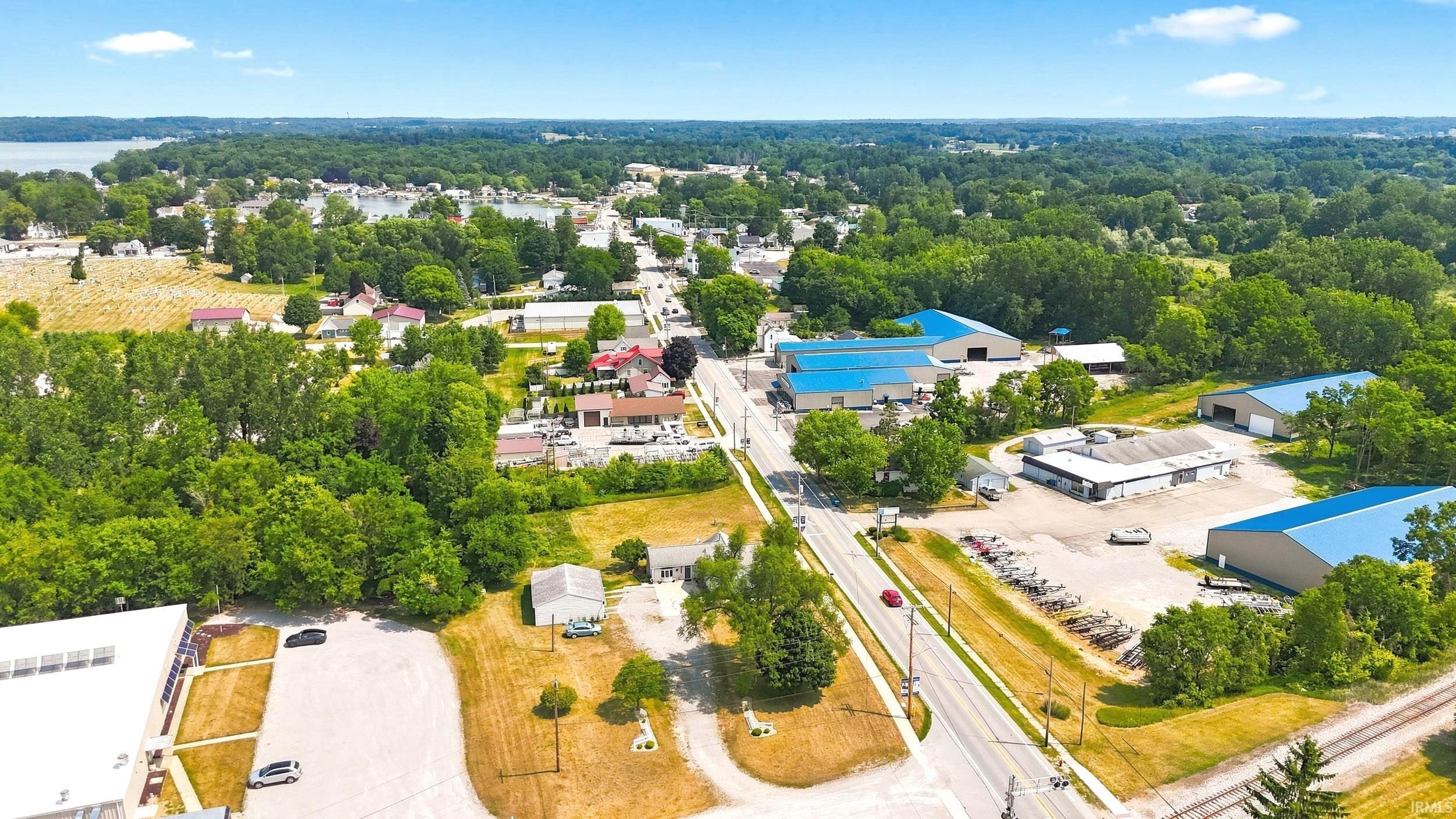 Aerial perspective showcasing a residential and commercial area with prominent mature trees, a visible body of water, and a paved road network