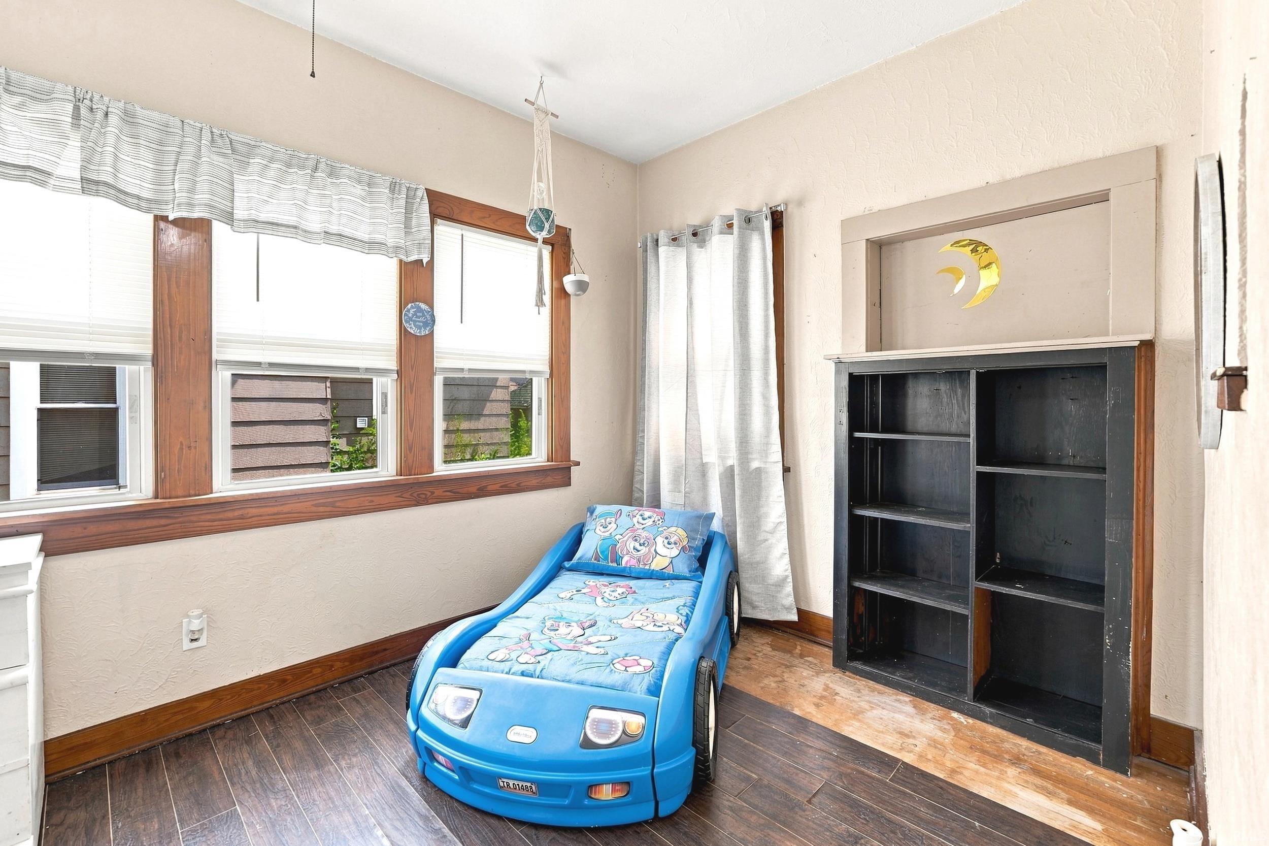 Wood-finish flooring with baseboard trim, three-panel window with wood framing, and a built-in shelving unit