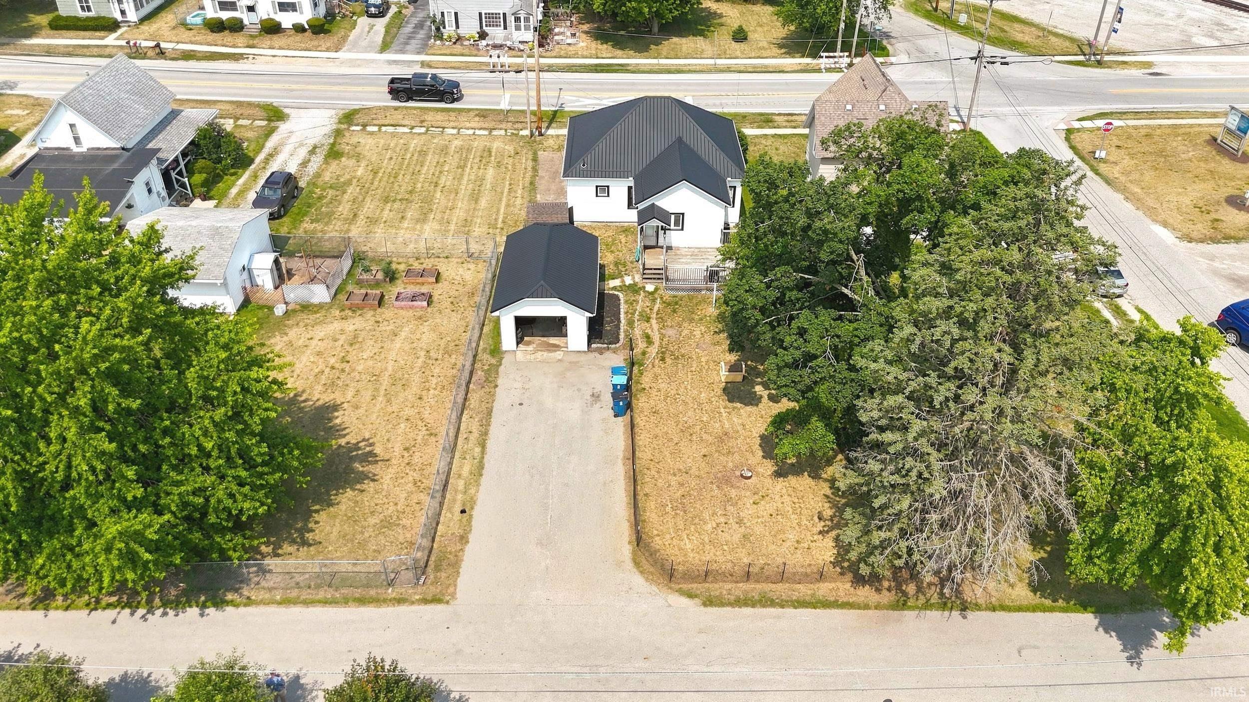 Aerial property view featuring a main residence with a dark roof, a detached garage with a dark roof, and mature perimeter trees