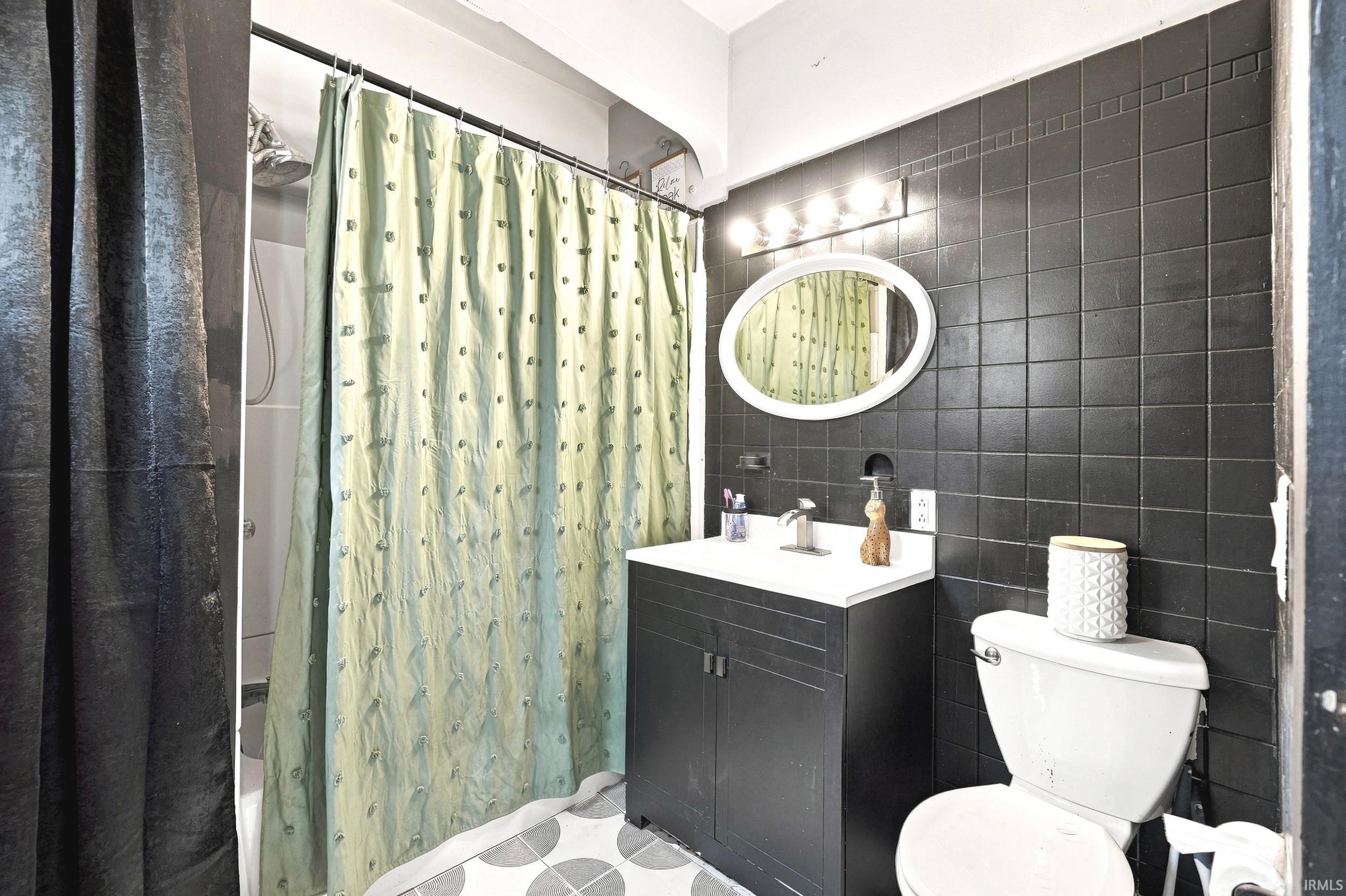 Bathroom featuring dark tile walls, an oval mirror, and a vanity with a white basin