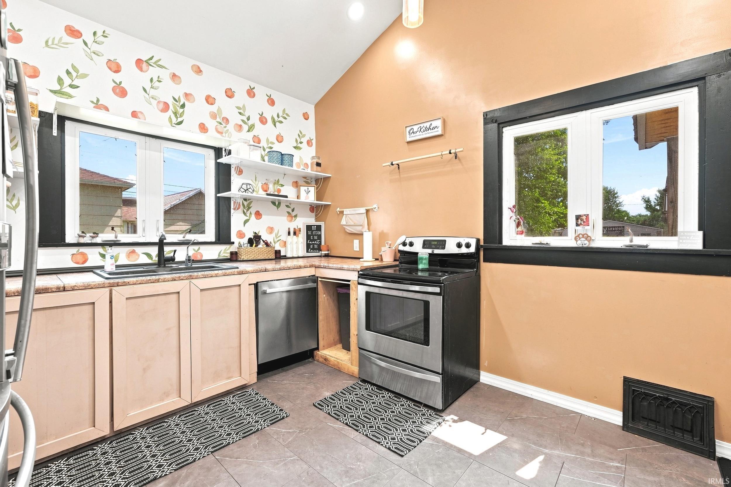 Open-concept kitchen featuring tile flooring, light wood cabinetry, stainless steel appliances, and a vaulted ceiling