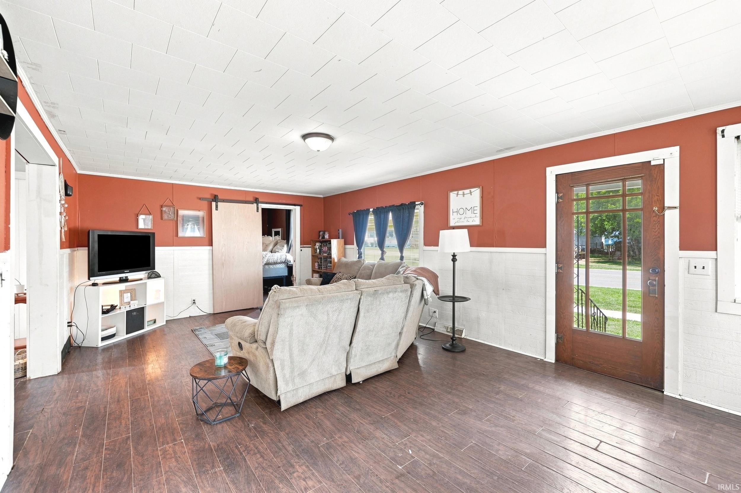 Expansive living area featuring wood-finish flooring, white wainscoting, and a white paneled ceiling