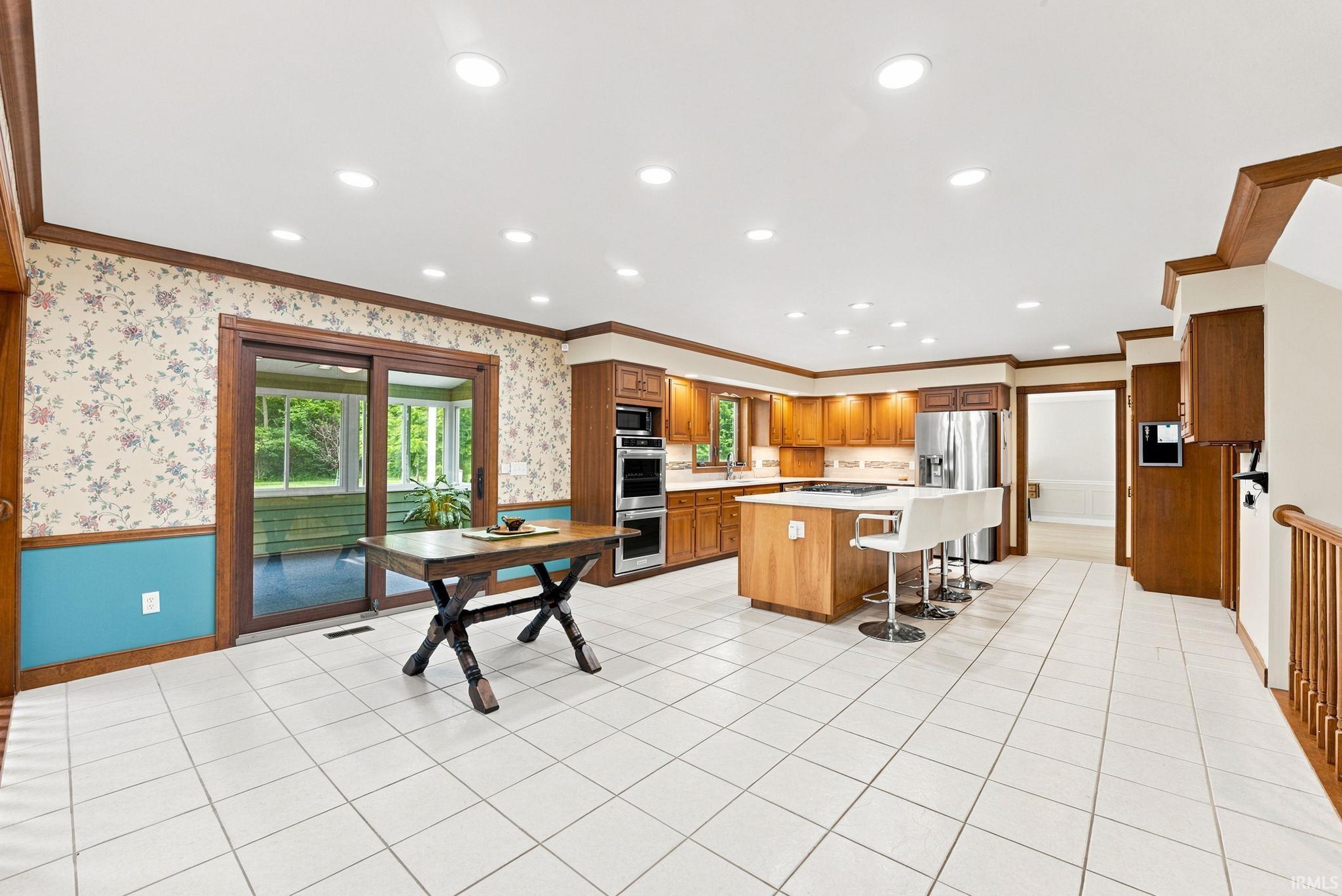Spacious kitchen featuring white tile flooring, recessed lighting, wood cabinetry, a central island, and stainless steel appliances