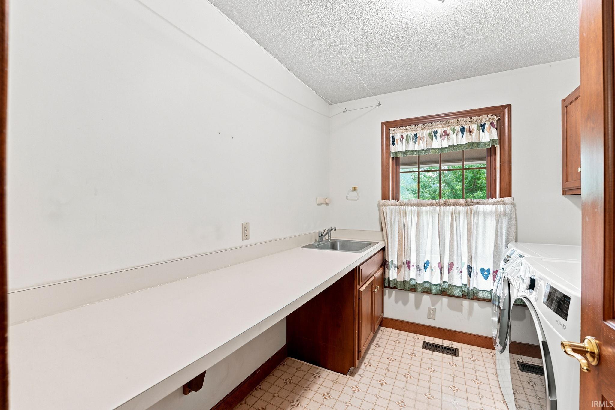 Laundry room featuring a deep utility sink, extensive white countertop space, and lower wood cabinetry