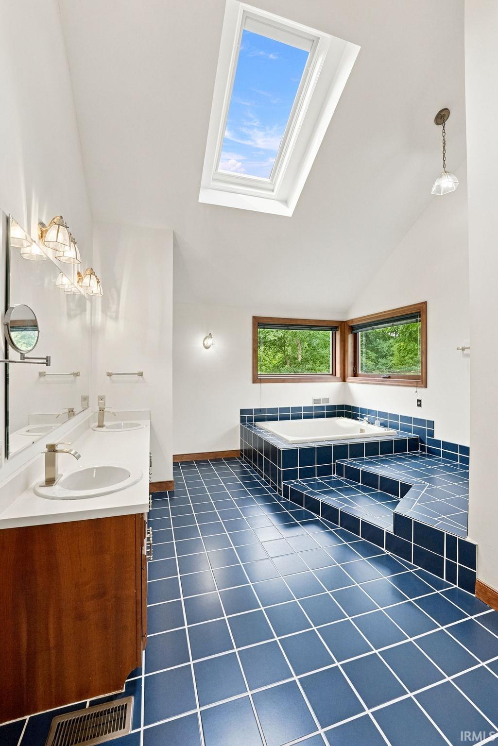 Bathroom with vaulted ceiling, large skylight, and blue square tile flooring