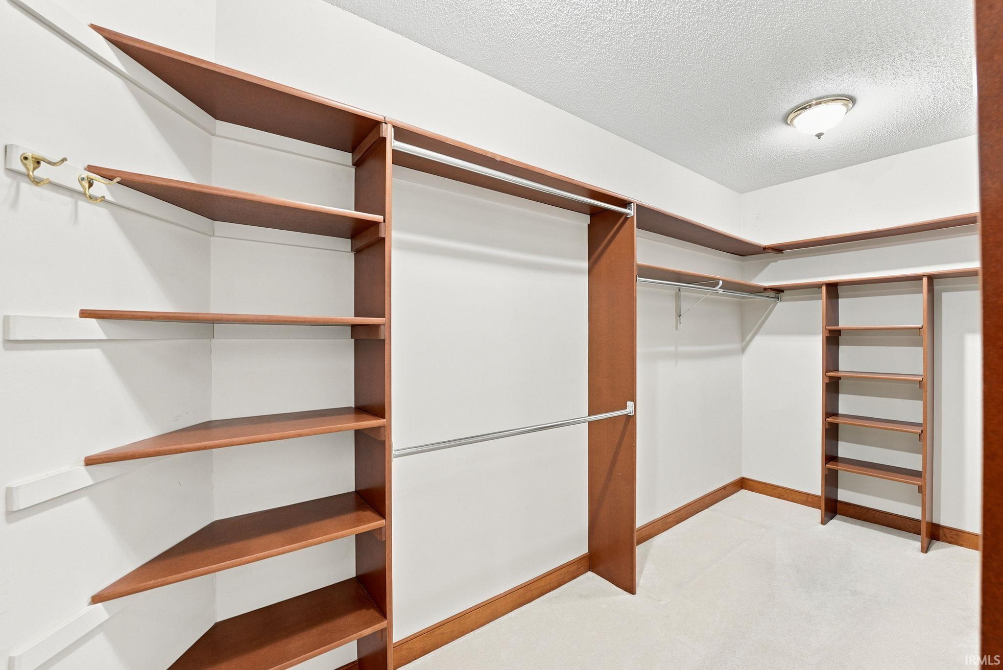 Walk-in closet featuring extensive built-in shelving, multiple hanging rods, corner shelving units, and a ceiling-mounted light fixture