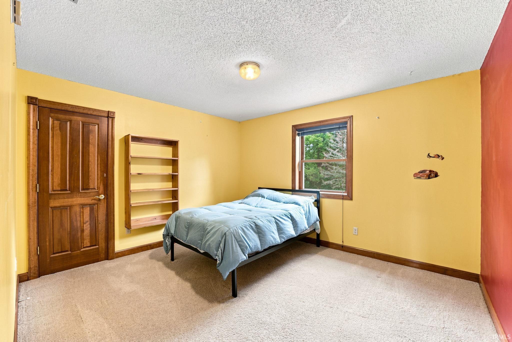 Carpeted room featuring a window with a wood-finish frame, a wood-finish door, and a built-in wood-finish shelving unit