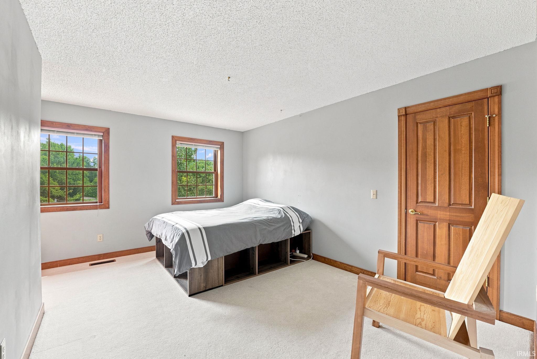 Bright bedroom featuring two windows with wood trim, a paneled wood door, light-colored carpeting, and light gray walls