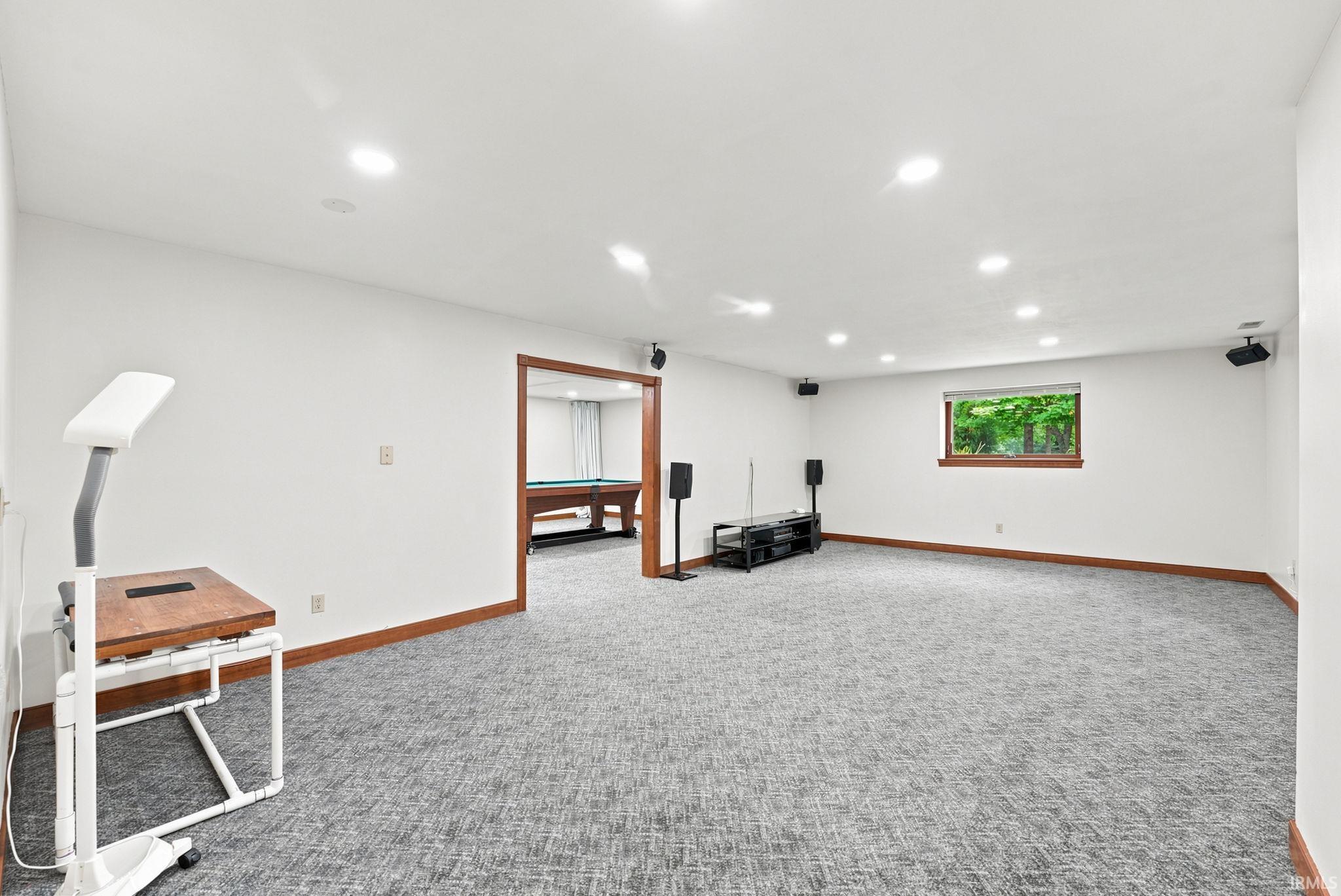Spacious entertainment area featuring recessed lighting, a window with wood trim, and textured gray carpeting