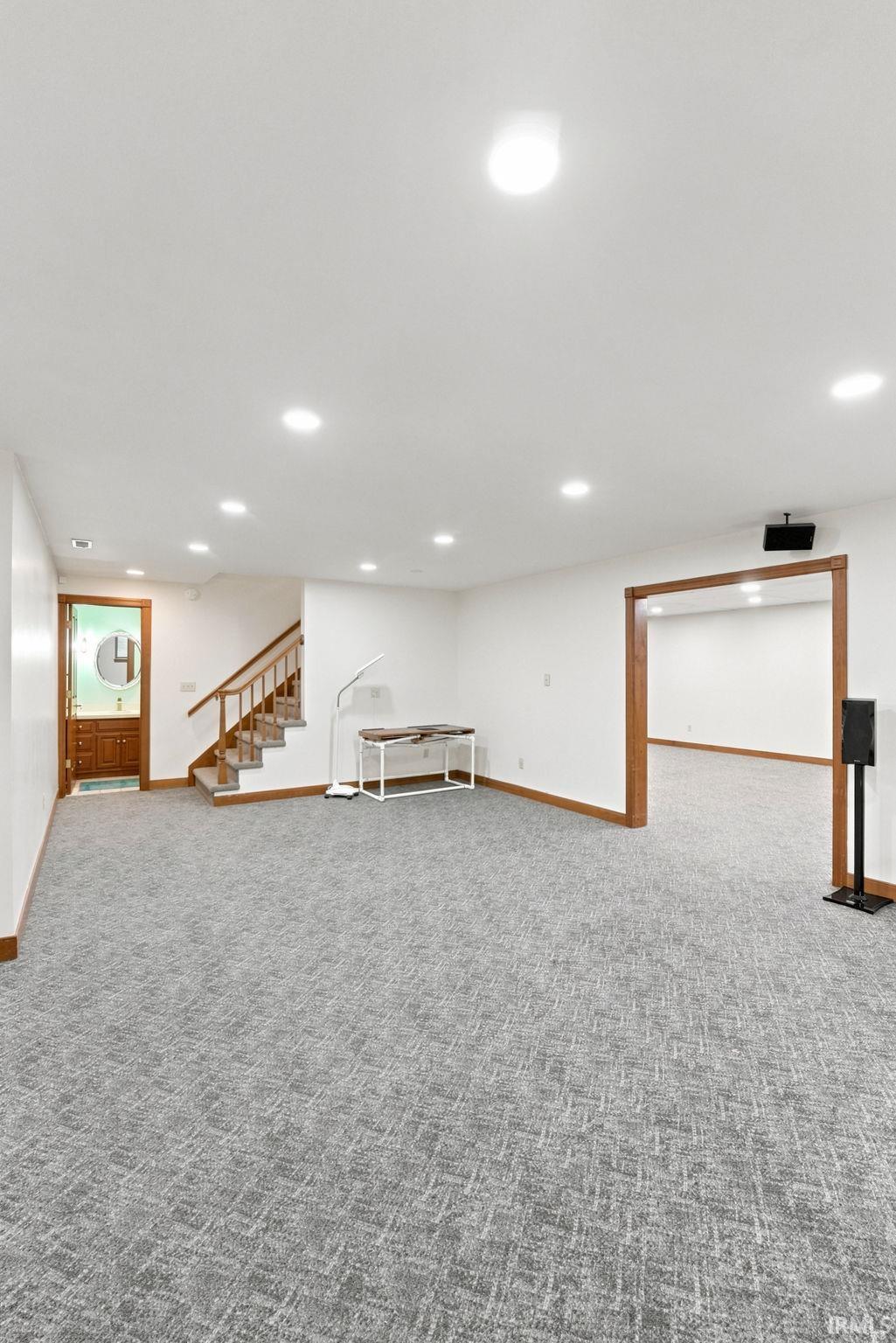 Spacious finished basement featuring patterned carpeting, recessed lighting, wood trim details, and a staircase with wood railings