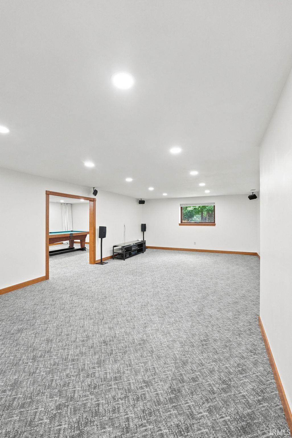Spacious carpeted room featuring recessed lighting, a framed doorway, and a window with wood trim