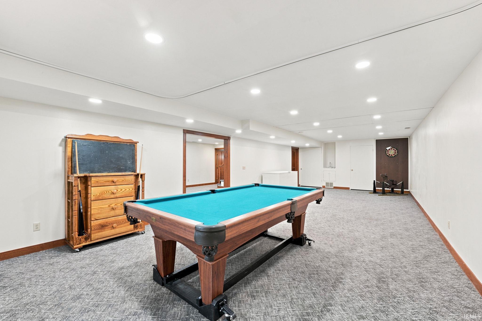 Spacious recreational room featuring recessed lighting, light gray textured carpeting, and white walls with wood-finish trim