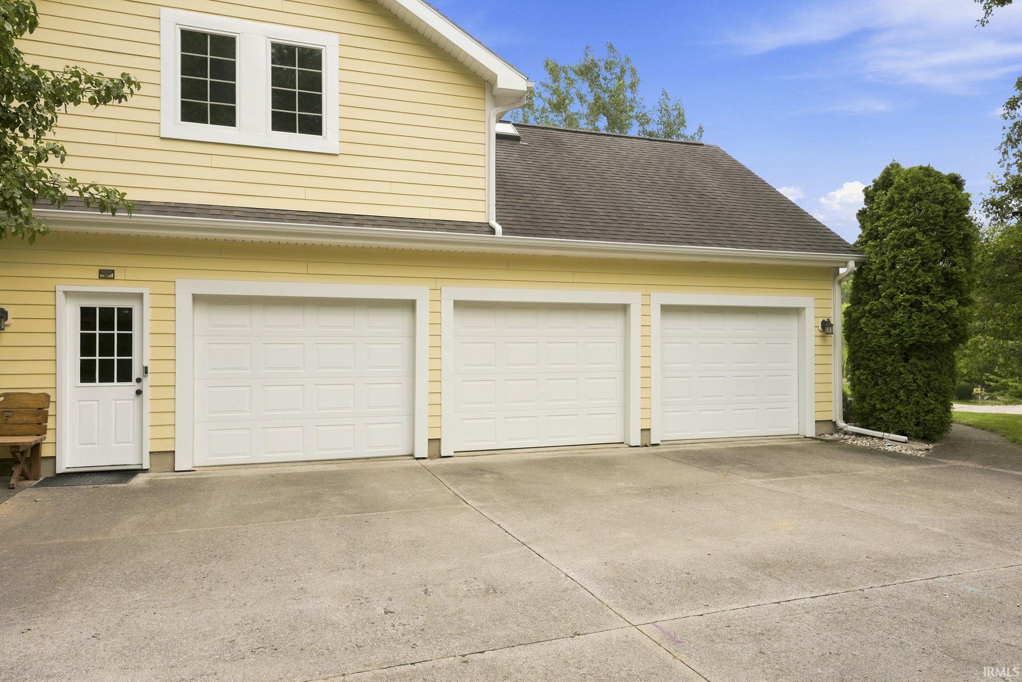 Three white panel garage doors with exterior lighting, a pedestrian entry door with glass lites, and yellow siding