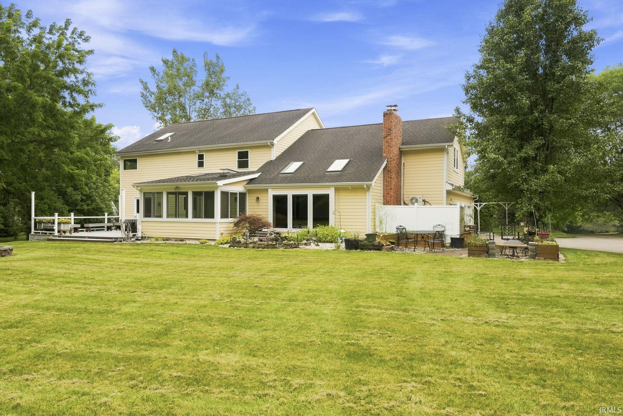 Expansive green lawn bordering a yellow-sided residence featuring a multi-level deck, a sunroom with numerous windows, and multiple skylights