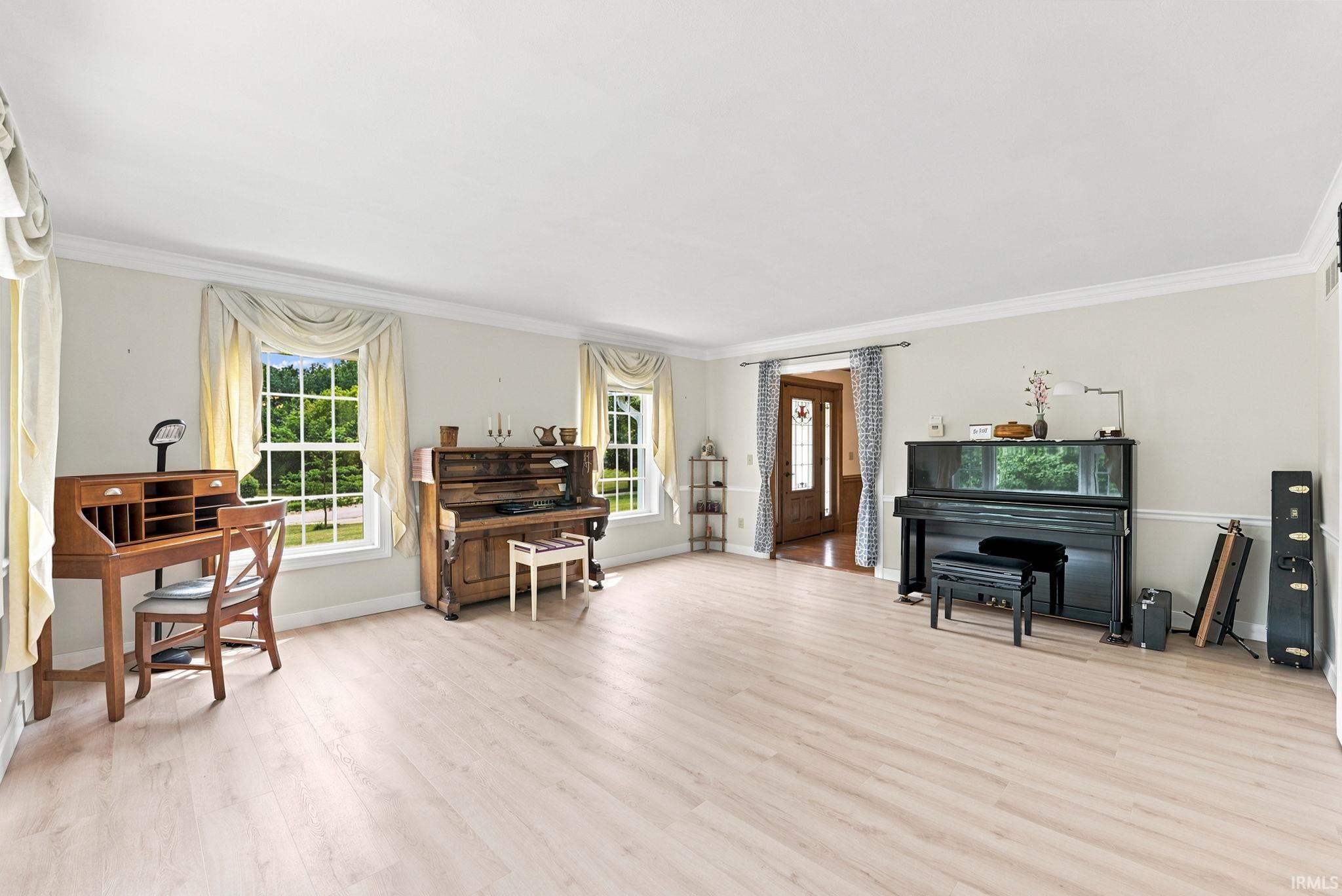 Spacious room featuring light wood-finish flooring, multiple pane windows, crown molding, and white baseboards
