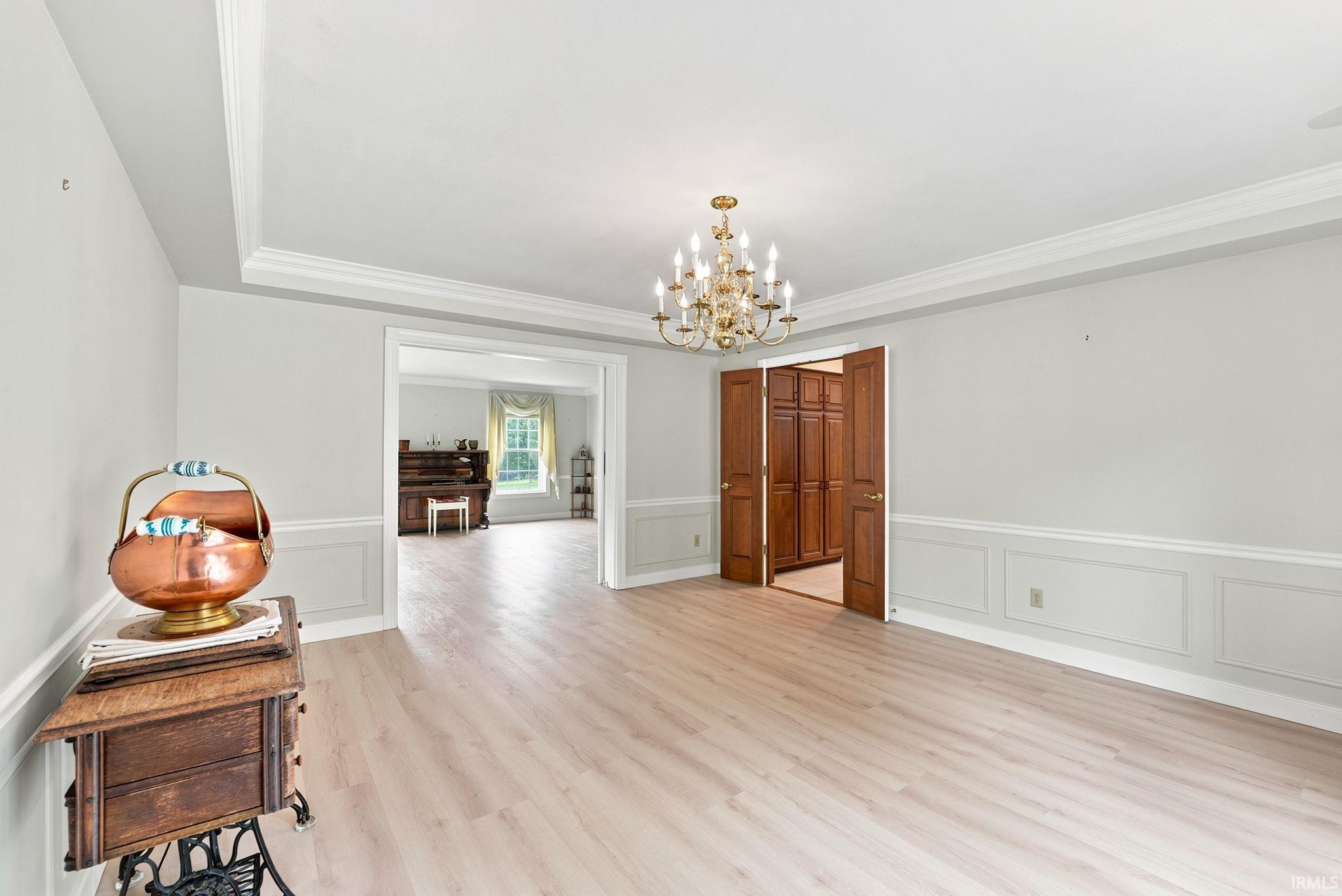 Spacious room featuring wood-finish flooring, wainscoting, and crown molding