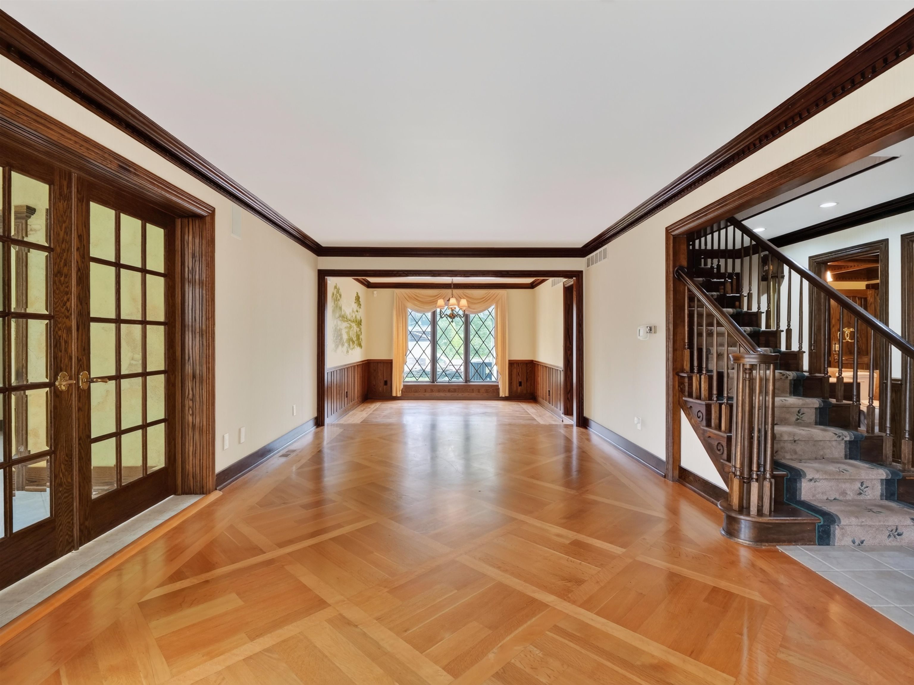 Expansive room featuring patterned wood-finish flooring, dark wood trim, and a grand staircase with carpeted treads